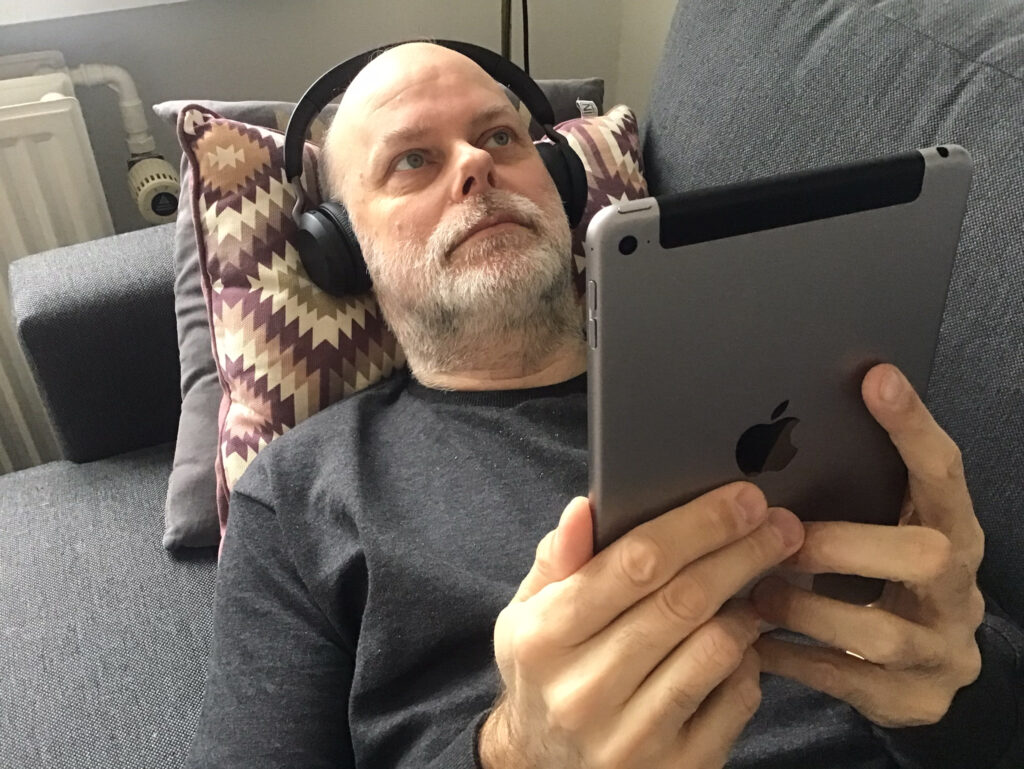 Kristian Marcussen liggende på sofa med iPad og hovedtelefoner